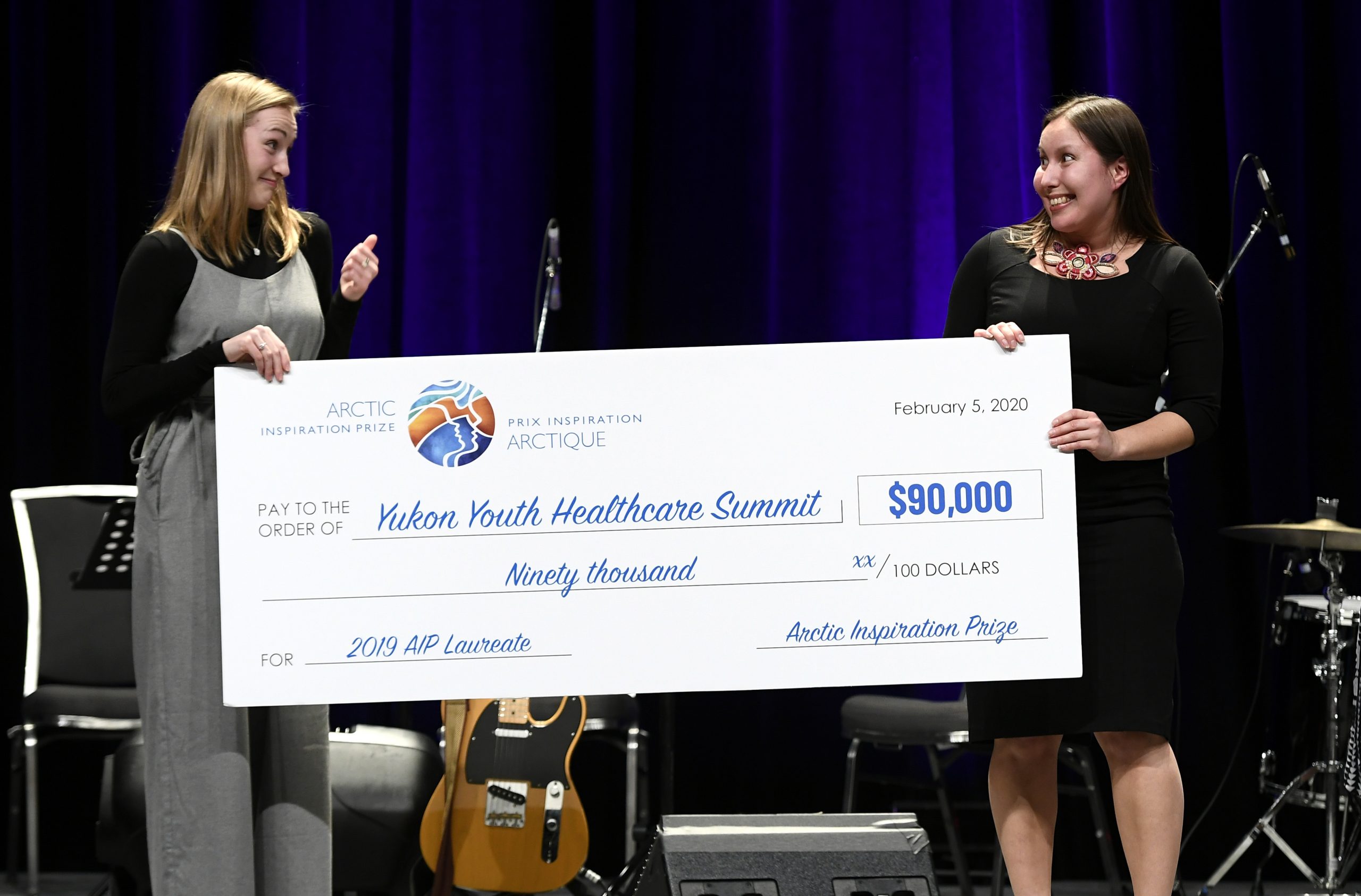 Two young women hold a large cheque for ninety thousand dollars. Deux jeunes femmes tiennent un chèque pour quatre-vingt dix milles dollars.