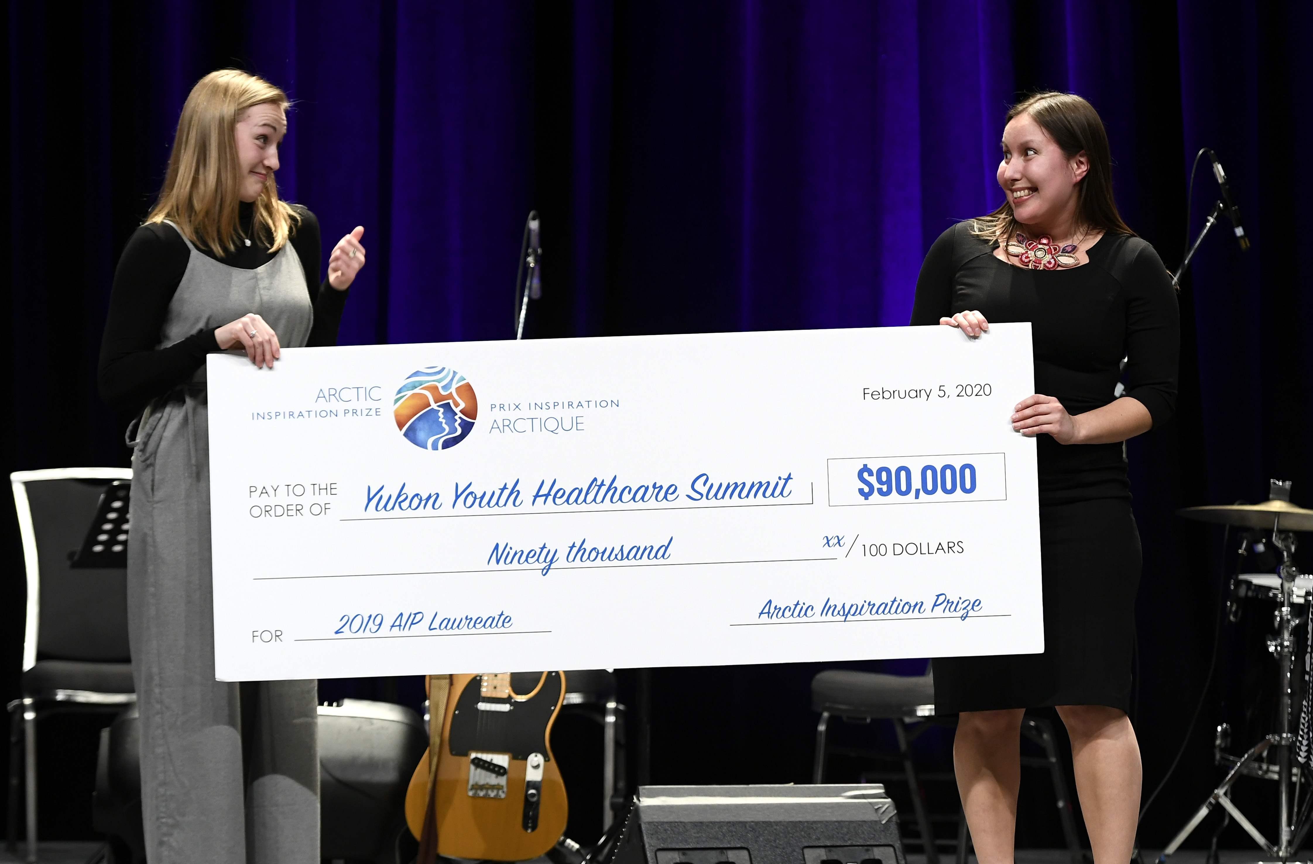 Two young women hold a large cheque for